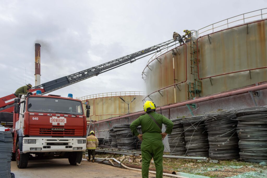Miembros de comandos de bomberos del territorio mantienen vigilancia sobre el tanque de combustible (crudo nacional) incendiado en la mañana del viernes último